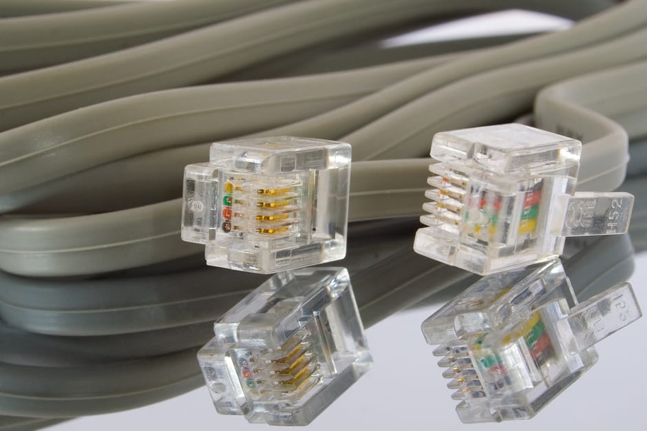 A close-up view of several grey Ethernet cables, neatly coiled and layered on top of each other, with four transparent RJ45 connectors featuring gold contacts and colored wiring visible inside. The ca